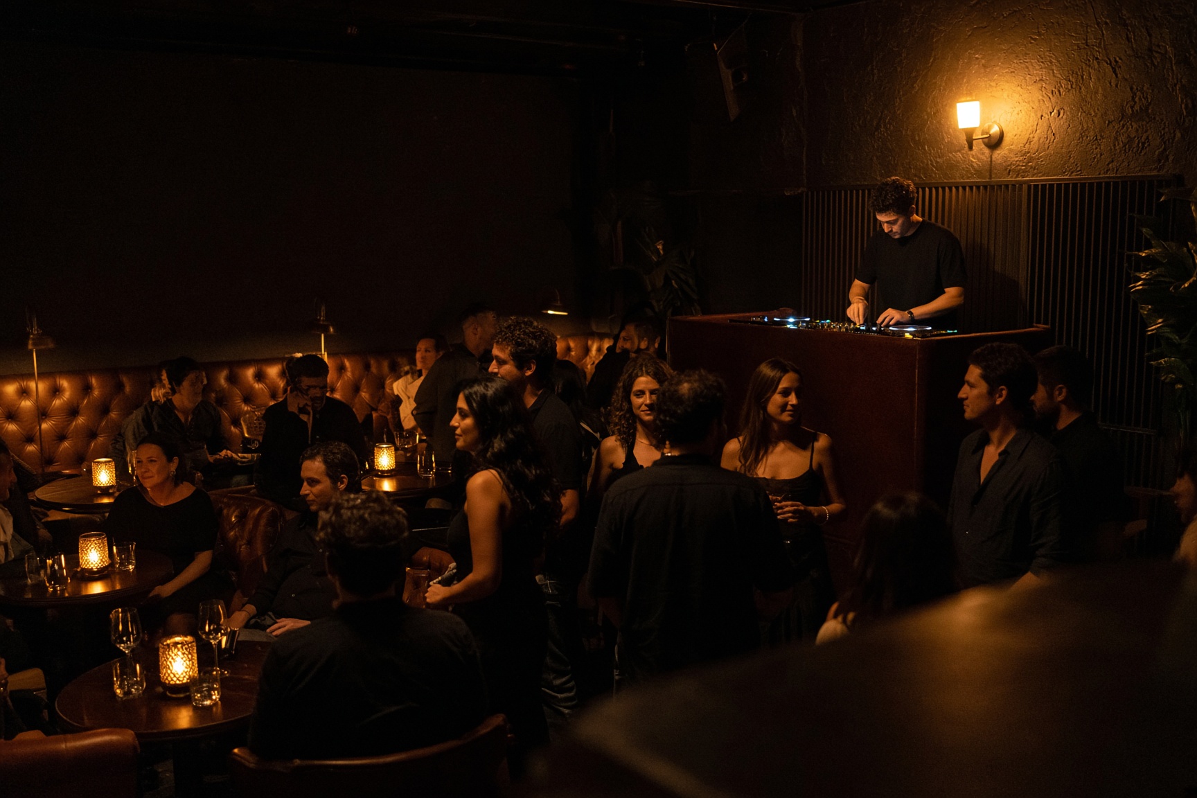 Intimate cocktail lounge with a DJ mixing for a standing crowd